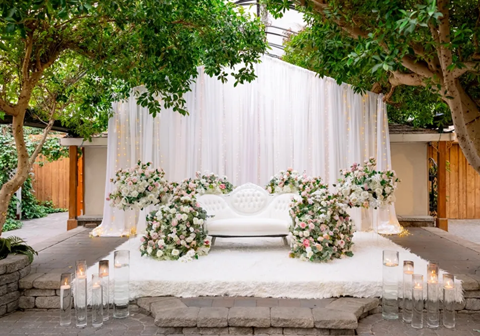 白いラグとラブシート、ピンクと白の花のアレンジメントで装飾された屋外結婚式会場のステージ