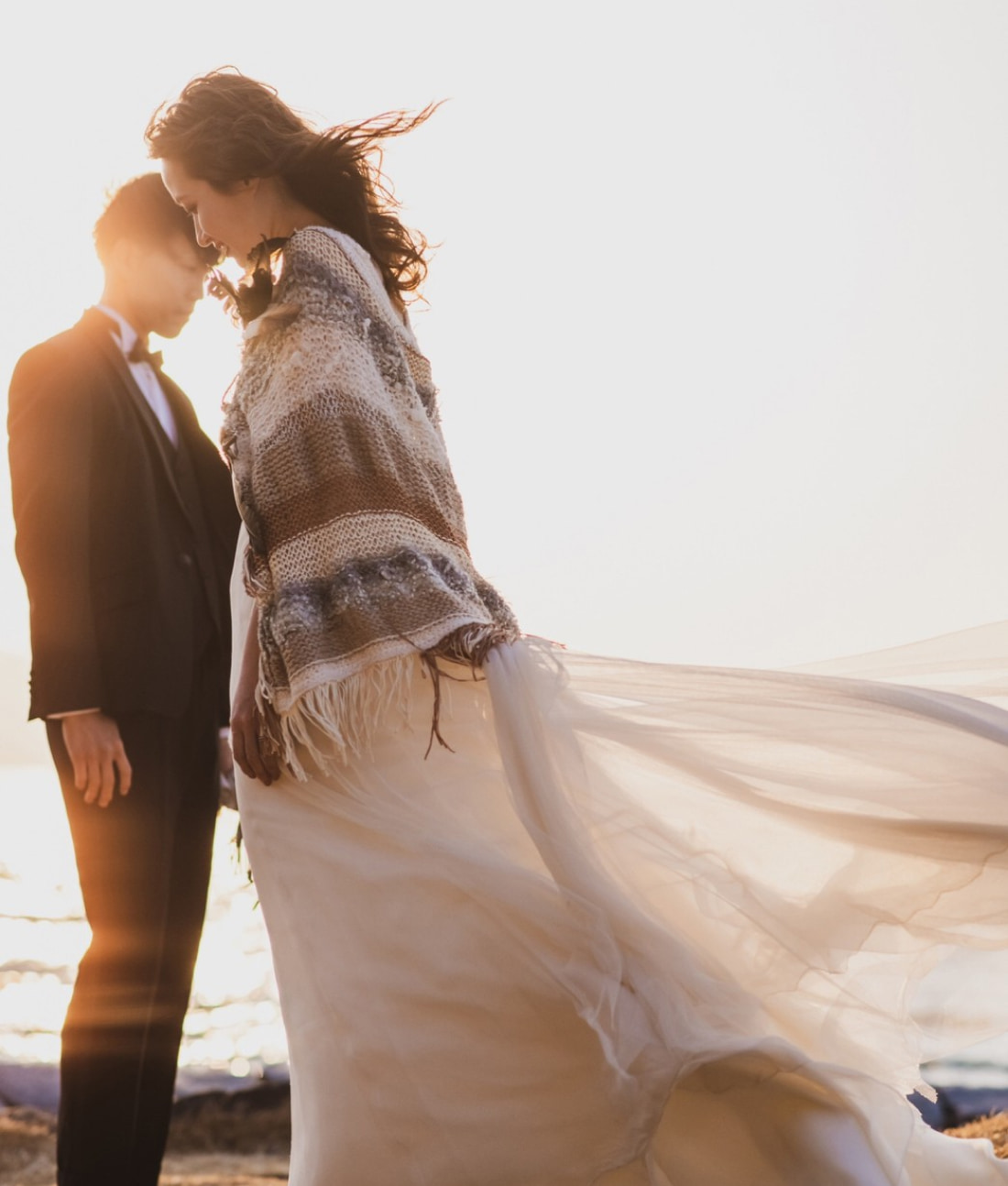 花嫁のドレスとショールが風になびき、陽光がふたりを暖かく包み込む。.