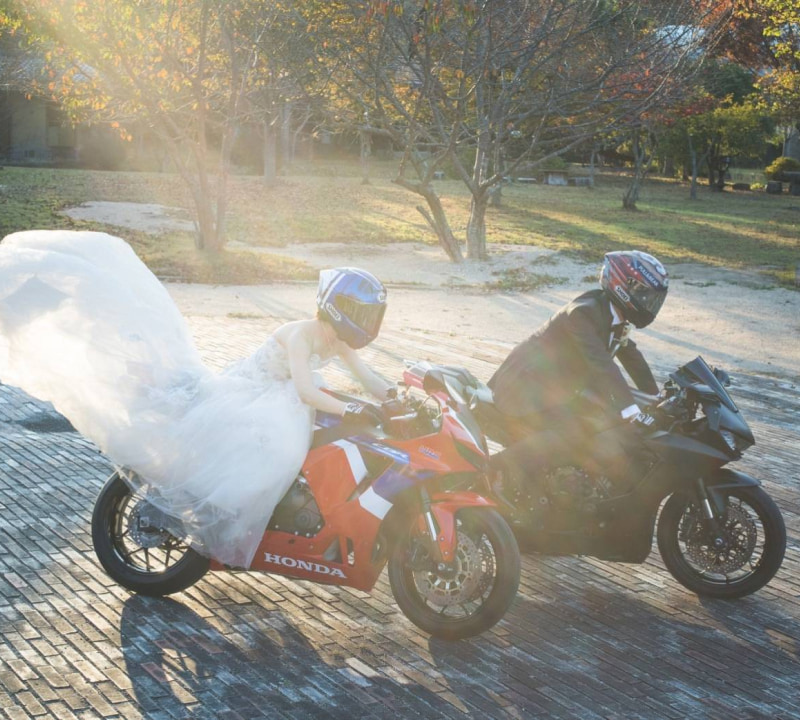 ウェディングドレスを着た女性とタキシードを着た男性がバイクに乗っているシーン。