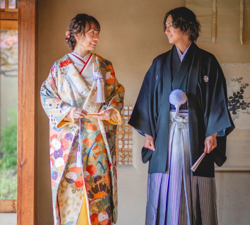 色とりどりの着物を着た女性と男性が対面している様子。女性は華やかな模様の着物を着用し、男性は伝統的な和装を身に着けている。