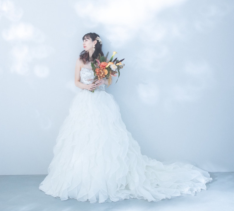 白いフリルのウエディングドレスを着た女性が花束を持ち、静かに立っている。