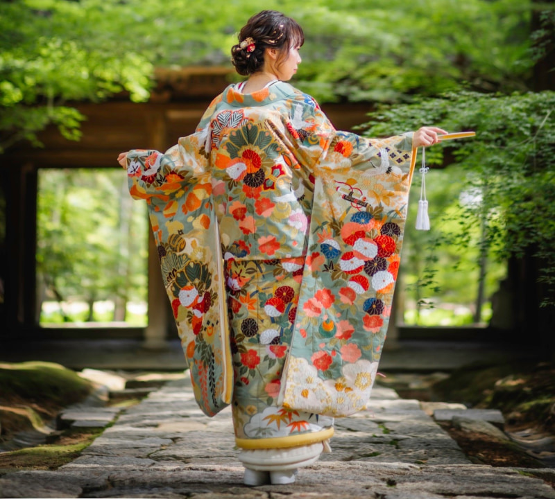色とりどりの花柄の着物を着た女性が後ろを向いている。着物の袖には華やかな模様が施されている。