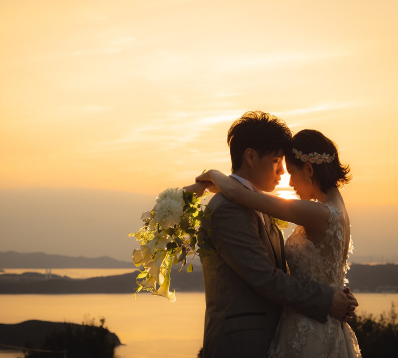 夕日を背景にした新郎新婦が抱き合い、花束を持つシーン。二人は互いに見つめ合っている。