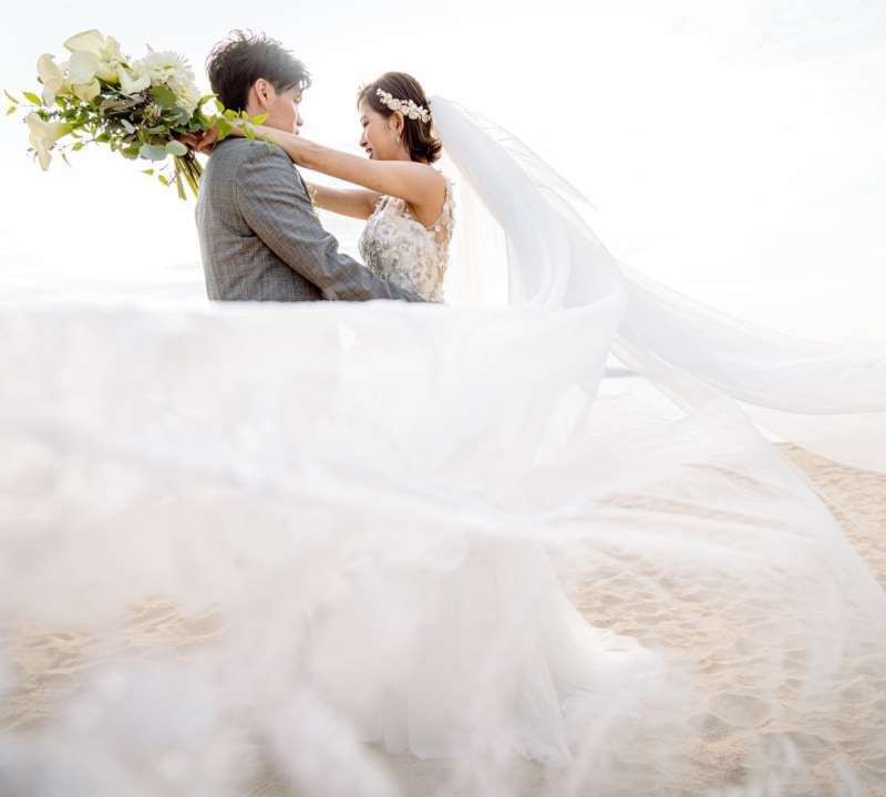 ビーチでウェディングドレスを着た新婦とタキシードを着た新郎が抱き合っているシーン。
