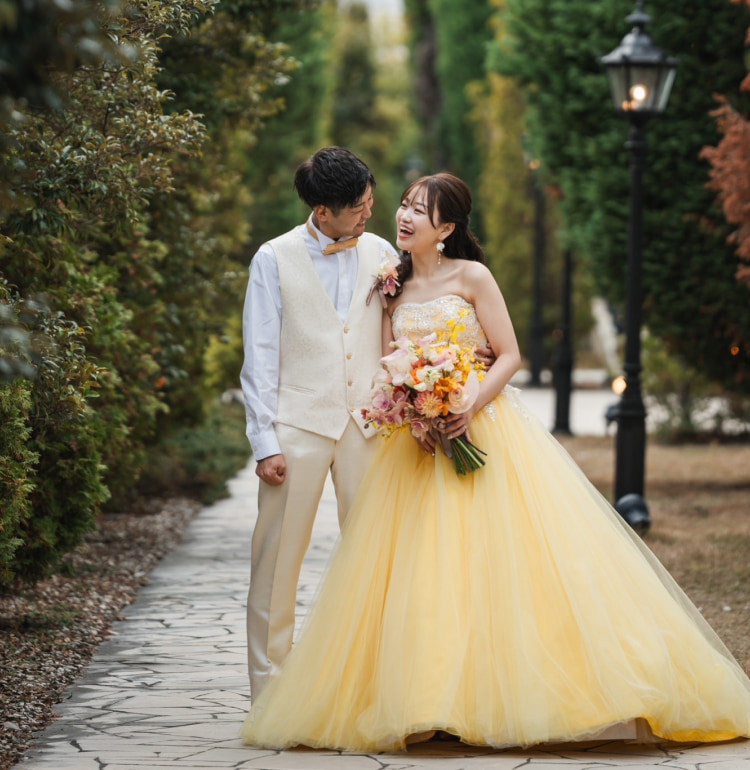 黄色のウエディングドレスを着た新婦と、白いベストを着た新郎が笑顔で向き合うシーン