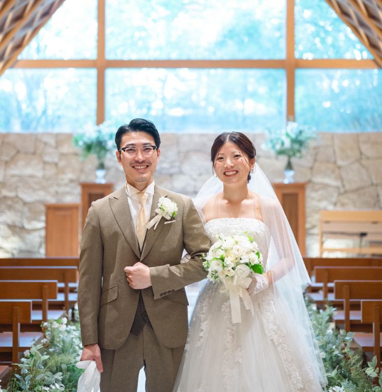 結婚式の新郎新婦が教会で並んで立っている。新婦はウェディングドレスを着用し、ブーケを持っている。