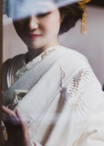 白い着物を着た女性の上半身。着物には刺繍が施され、髪には装飾がある。