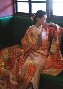 華やかな色合いの着物を着た女性がソファに座っている。着物には大きな花柄が描かれている。