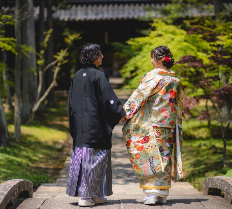 和装を着た二人が手をつないで歩いている様子。色とりどりの着物と黒い羽織が特徴的。
